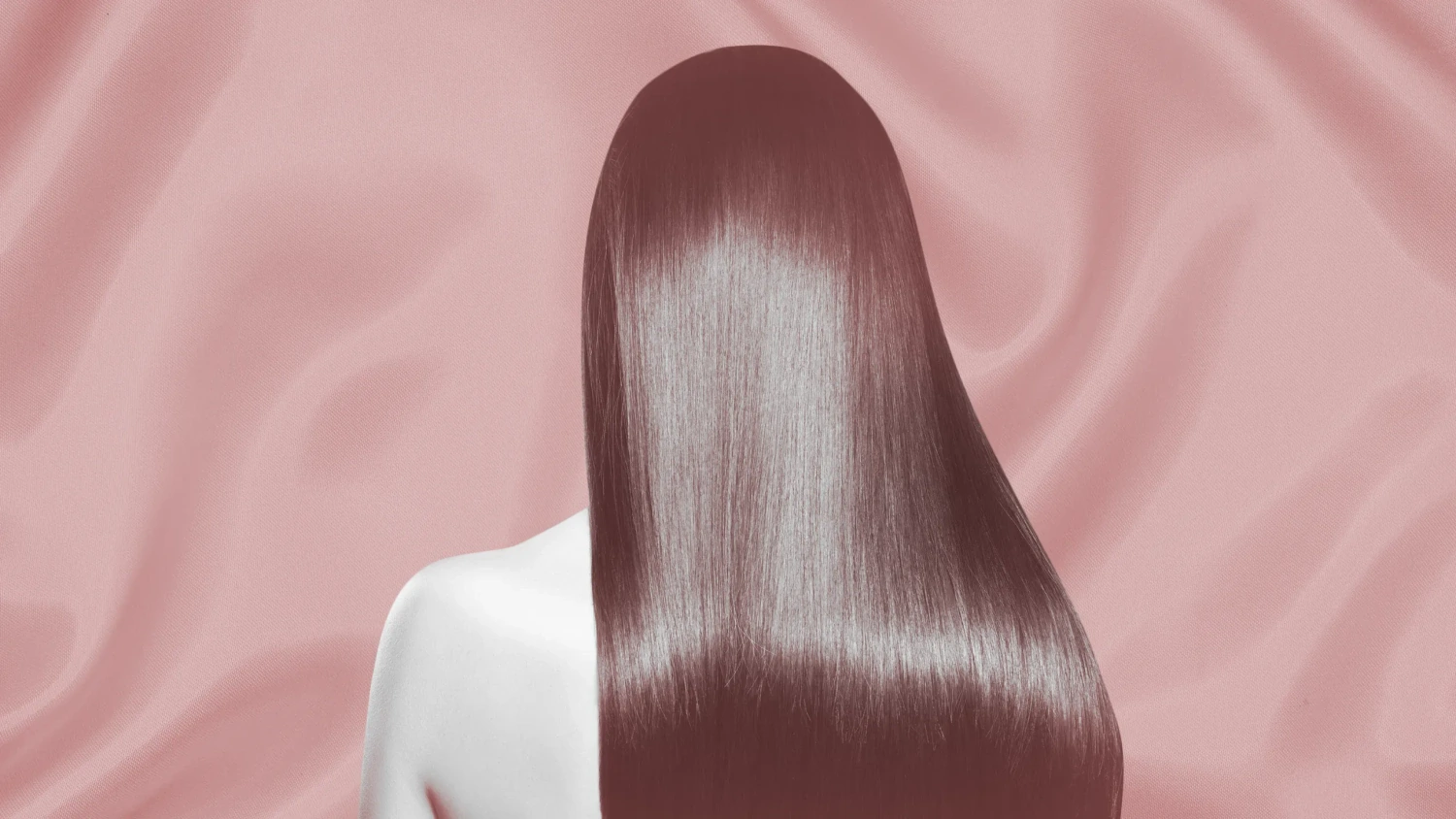 A person with shiny, straight, long brown hair is shown from behind against a silky, soft pink background. The smooth hair reflects light, emphasizing its healthy, glossy texture. The person’s shoulder is partially visible and their skin is fair.