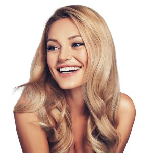 A young woman with long, wavy blonde hair and clear skin smiles brightly to the side against a white background. Her hair shines after using Gel Keratin Treatment, and her cheerful expression suggests confidence in her smooth locks.