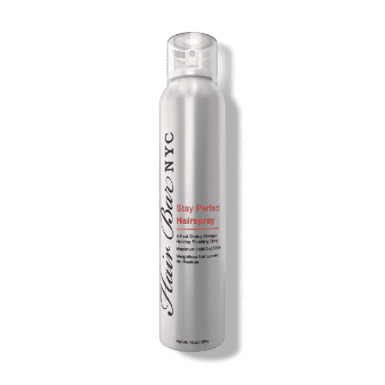 A sleek silver aerosol can of Stay Perfect hairspray stands upright, featuring black and red text for branding and product details. The design is modern with a translucent cap.
